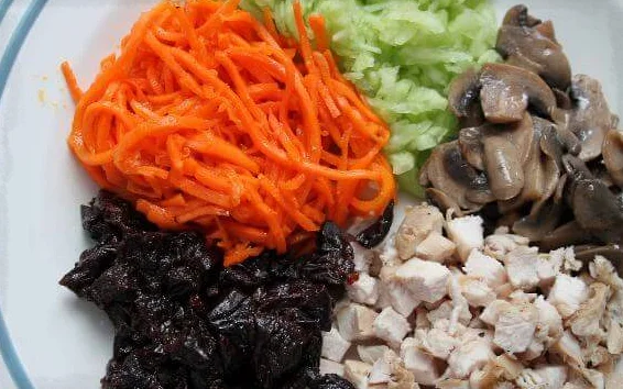 Подготовленные продукты для салата с курицей, черносливом и корейской морковью на большой тарелке