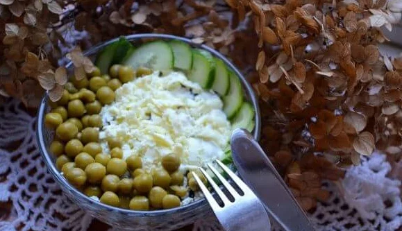 Салат с курицей, черносливом и консервированным горошком в маленьком салатнике с металлическими столовыми приборами
