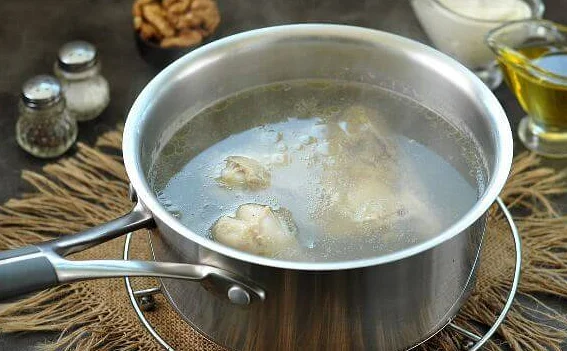 Кусочек курицы и бульон в металлической кастрюле с ручкой на столе