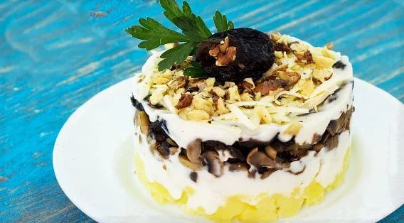 Порция салата с курицей, черносливом и картофелем на белой тарелке