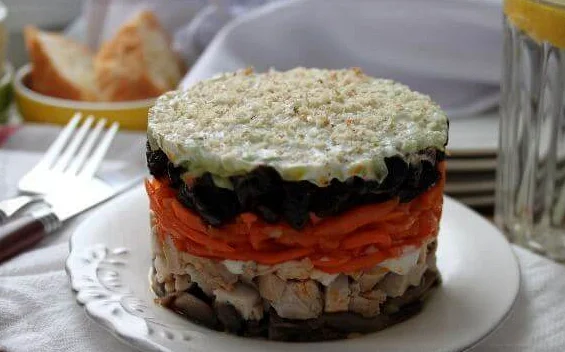 Слоёный салат с курицей, черносливом и морковью по-корейски на сервированном столе